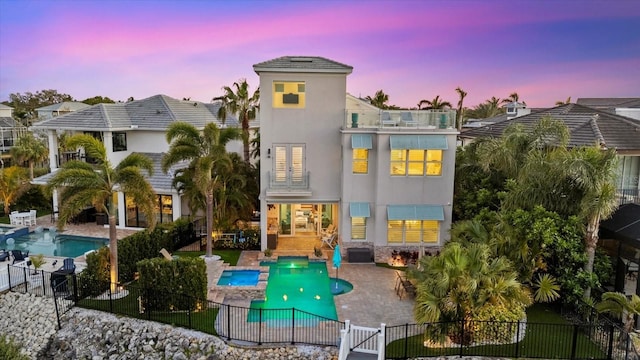 back of house at dusk with a patio, a balcony, a gate, stucco siding, and fence private yard