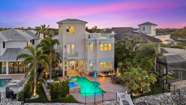 back of house at dusk featuring stucco siding, a patio, a fenced backyard, glass enclosure, and a balcony