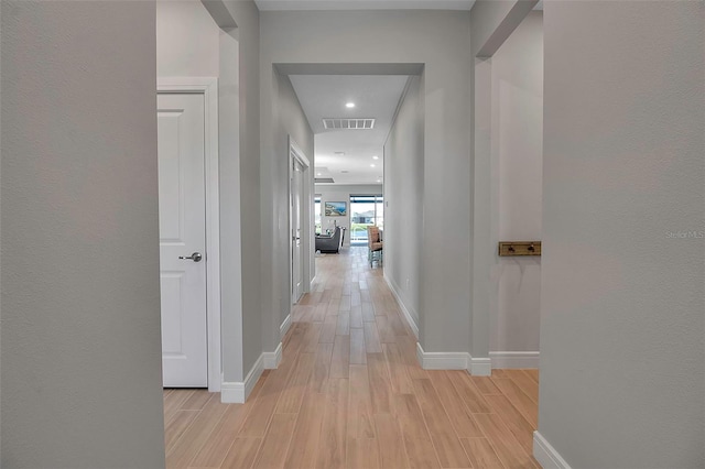 hall with light wood finished floors, visible vents, and baseboards