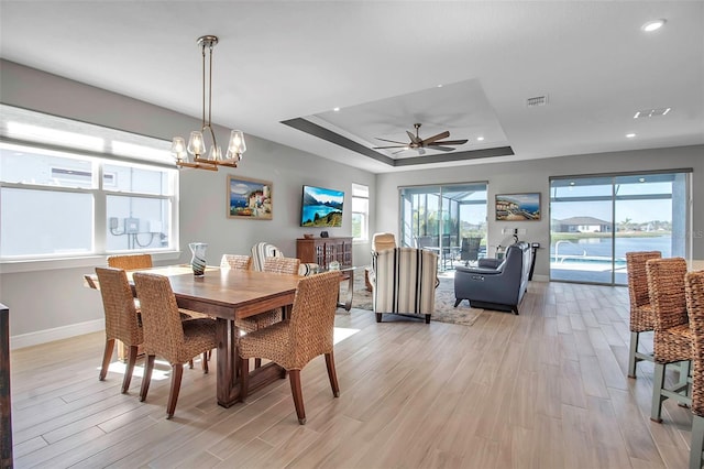 dining room featuring baseboards, a raised ceiling, ceiling fan with notable chandelier, and light wood finished floors