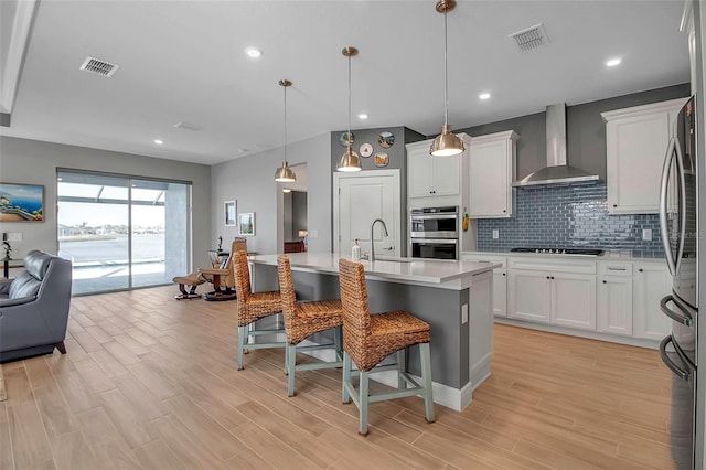 kitchen with wall chimney range hood, a breakfast bar area, visible vents, and stainless steel appliances