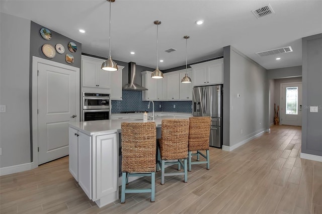 kitchen with visible vents, decorative backsplash, light countertops, appliances with stainless steel finishes, and wall chimney exhaust hood