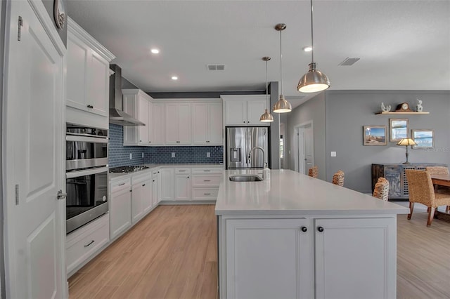 kitchen with a sink, stainless steel appliances, visible vents, and wall chimney range hood