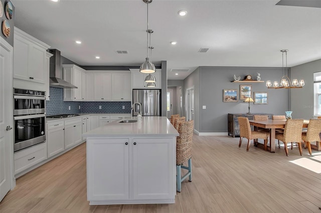 kitchen featuring visible vents, a sink, stainless steel appliances, light countertops, and wall chimney exhaust hood