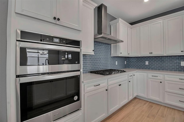 kitchen featuring wall chimney range hood, light countertops, decorative backsplash, stainless steel appliances, and white cabinetry