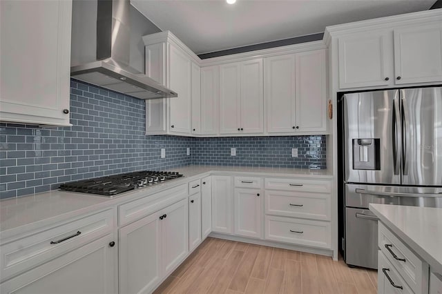 kitchen featuring tasteful backsplash, light countertops, appliances with stainless steel finishes, white cabinetry, and wall chimney exhaust hood