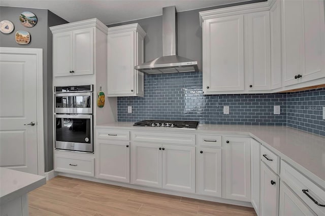 kitchen featuring backsplash, white cabinetry, stainless steel appliances, wall chimney exhaust hood, and light countertops