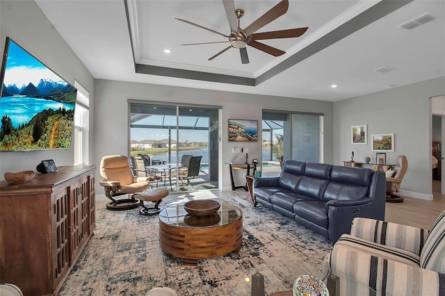 living area with visible vents, baseboards, ceiling fan, ornamental molding, and a raised ceiling