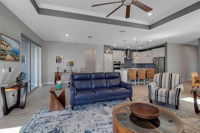 living area featuring light wood-type flooring, crown molding, and a tray ceiling