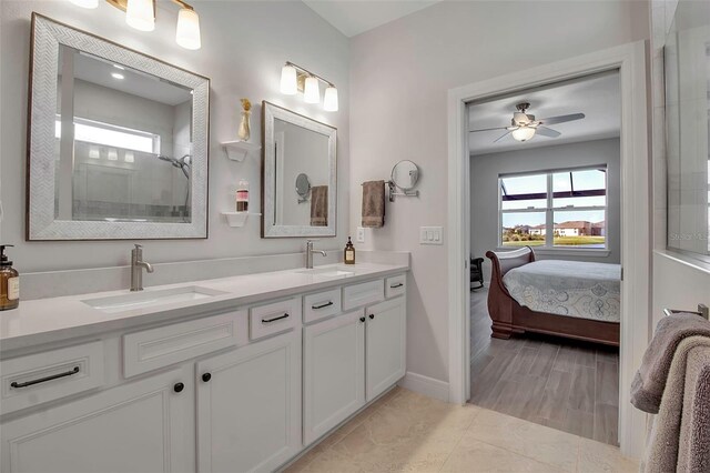 ensuite bathroom with double vanity, tiled shower, a ceiling fan, and a sink