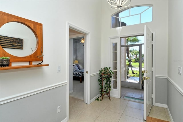 entryway featuring light tile patterned flooring, baseboards, a towering ceiling, and a chandelier