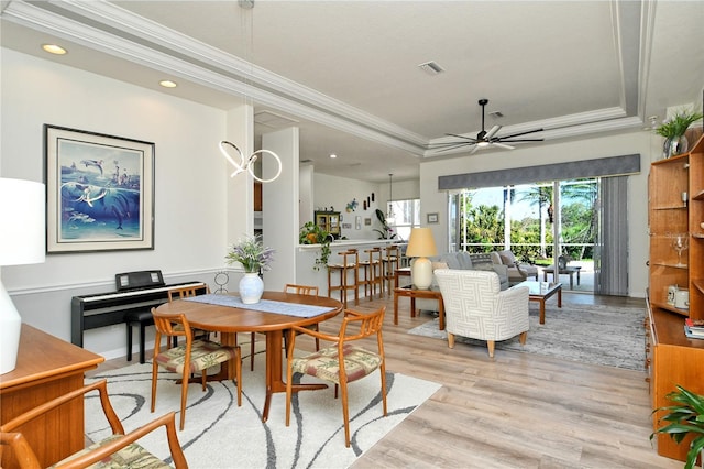 dining space featuring visible vents, crown molding, ceiling fan, light wood-type flooring, and a raised ceiling