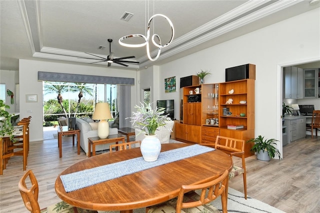 dining area featuring a tray ceiling, ceiling fan with notable chandelier, ornamental molding, and light wood finished floors