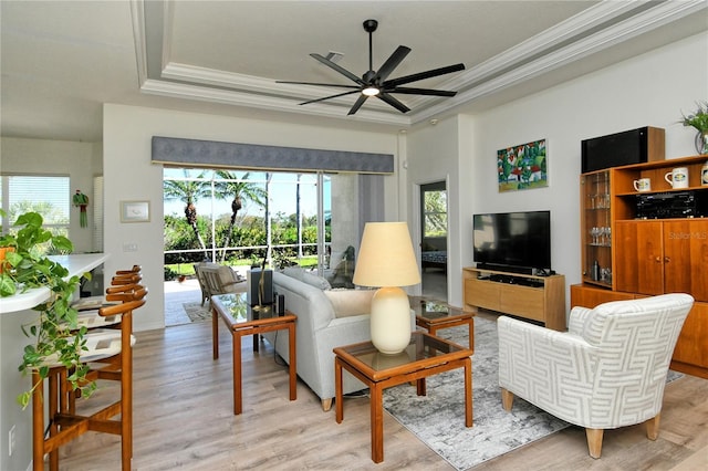 living room with light wood finished floors, a tray ceiling, a ceiling fan, and ornamental molding