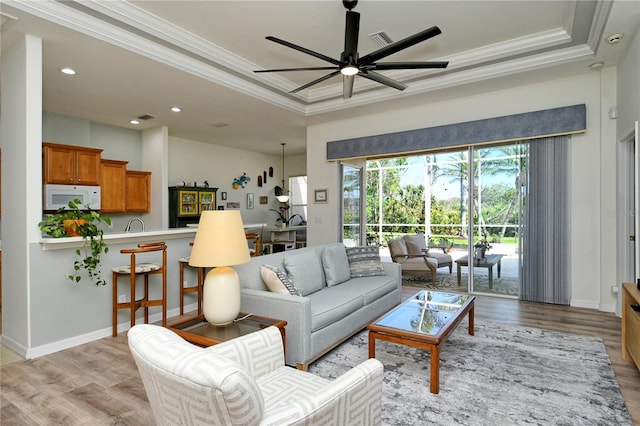 living area with crown molding, light wood-style floors, a tray ceiling, and ceiling fan