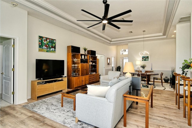 living room featuring light wood-type flooring, a raised ceiling, a ceiling fan, and crown molding