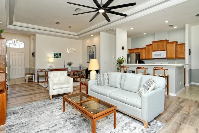 living room with a raised ceiling, ceiling fan with notable chandelier, visible vents, and light wood-type flooring