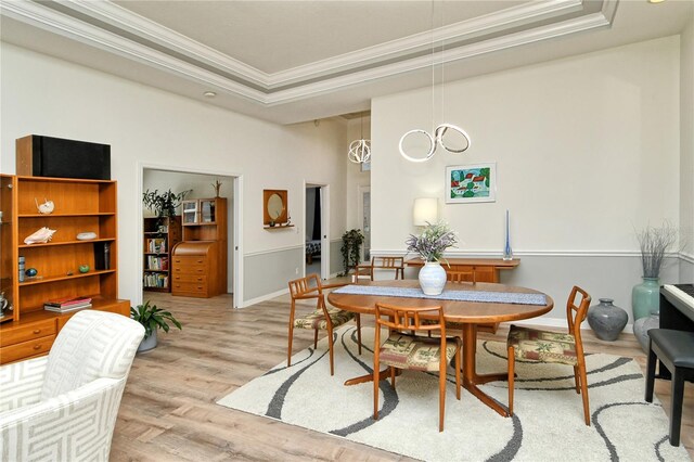 dining space featuring light wood-style flooring, ornamental molding, a tray ceiling, baseboards, and a chandelier