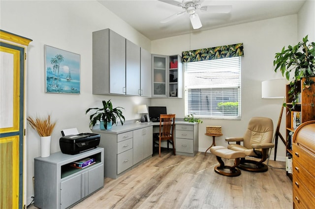 office featuring baseboards, built in desk, a ceiling fan, and light wood finished floors