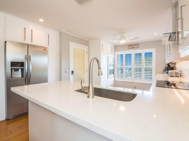 kitchen with a sink, light countertops, white cabinets, black electric stovetop, and stainless steel fridge