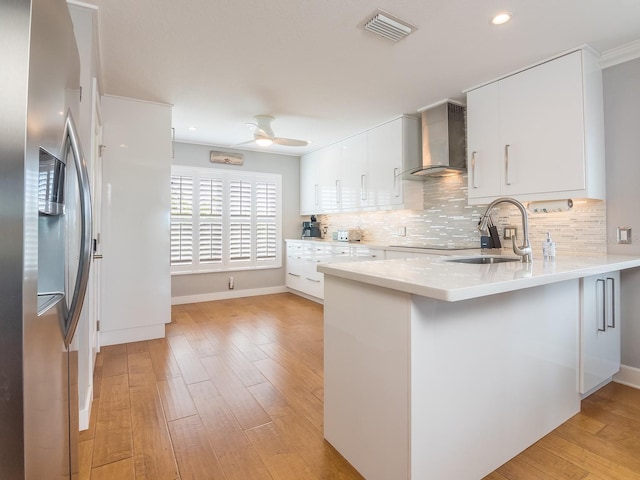 kitchen featuring a peninsula, stainless steel fridge, wall chimney exhaust hood, a ceiling fan, and a sink