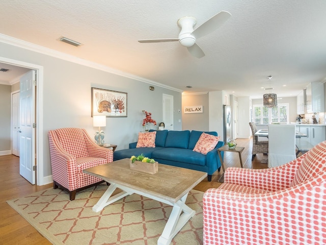 living area featuring ceiling fan, visible vents, light wood finished floors, and ornamental molding