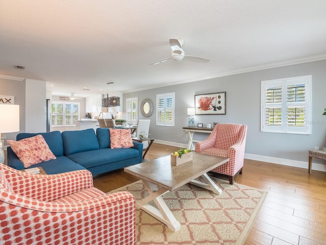 living area featuring hardwood / wood-style floors, visible vents, ornamental molding, and a ceiling fan