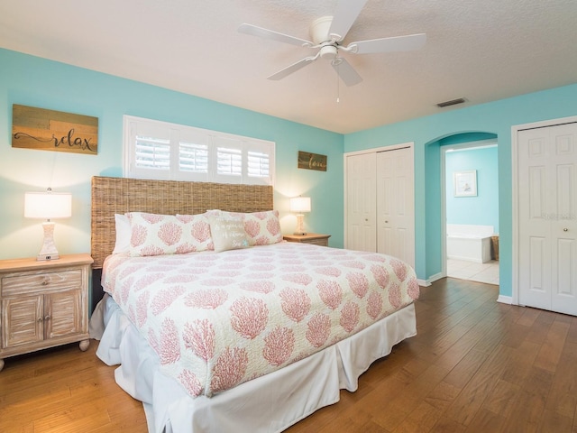 bedroom featuring arched walkways, visible vents, two closets, and wood finished floors