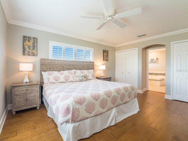 bedroom with wood finished floors, arched walkways, visible vents, and baseboards