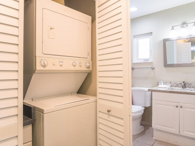 clothes washing area with a sink, laundry area, light tile patterned floors, and stacked washing maching and dryer