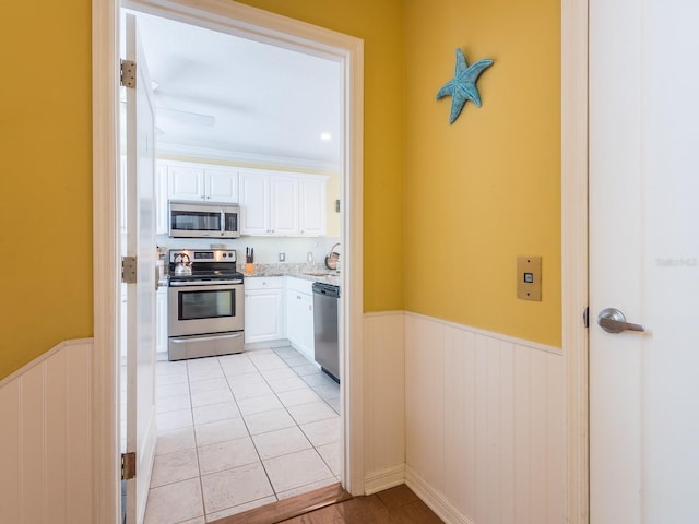 kitchen with white cabinets, light tile patterned floors, appliances with stainless steel finishes, and wainscoting