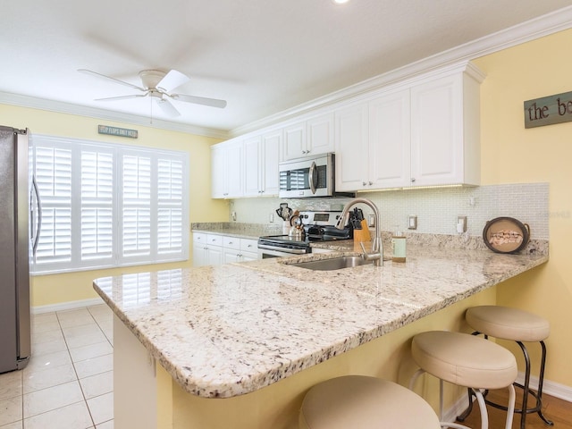 kitchen with a ceiling fan, a peninsula, a sink, appliances with stainless steel finishes, and tasteful backsplash