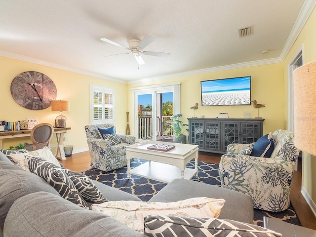 living room featuring wood finished floors, baseboards, visible vents, ceiling fan, and ornamental molding