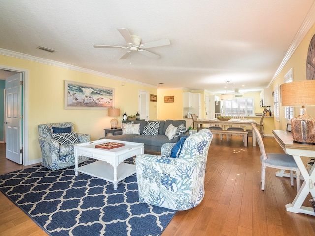 living room featuring a ceiling fan, visible vents, wood-type flooring, and ornamental molding