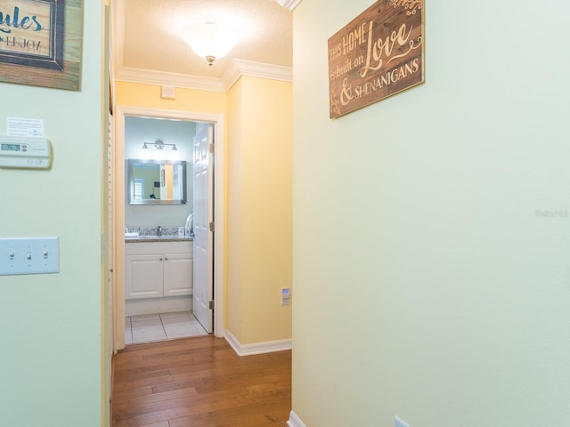 hallway featuring a sink, baseboards, crown molding, and light wood finished floors