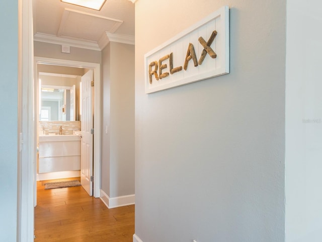 corridor with baseboards, wood finished floors, attic access, and ornamental molding