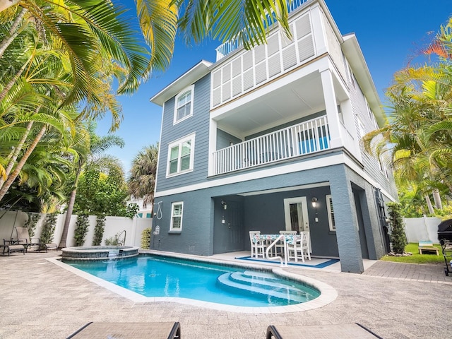 rear view of property with stucco siding, a pool with connected hot tub, a patio, a fenced backyard, and a balcony