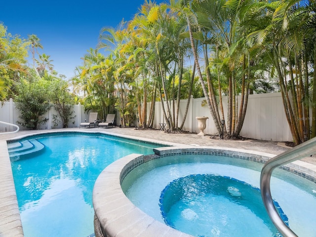 view of swimming pool with a fenced backyard and a pool with connected hot tub