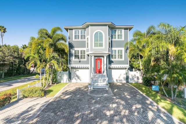 beach home with decorative driveway, a garage, and fence