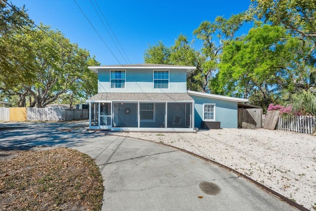 back of property with concrete driveway, fence, a sunroom, and stucco siding