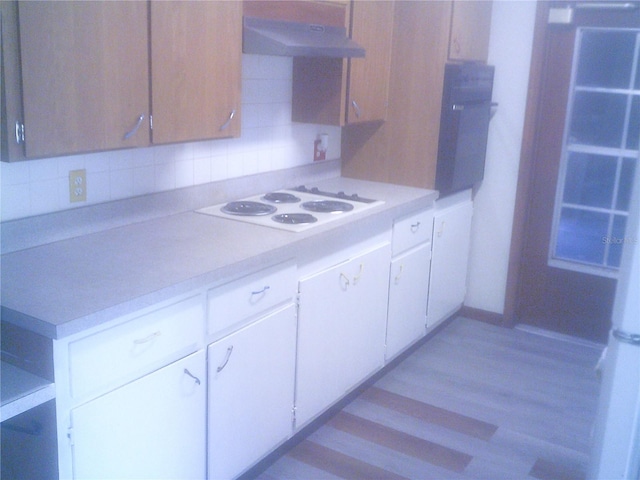 kitchen featuring white electric stovetop, light countertops, under cabinet range hood, white cabinetry, and backsplash