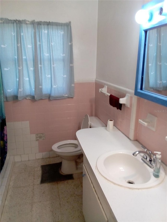 bathroom featuring tile walls, a wainscoted wall, toilet, and vanity