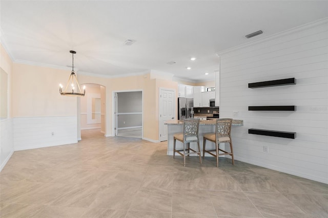 kitchen with ornamental molding, a peninsula, stainless steel appliances, arched walkways, and white cabinetry