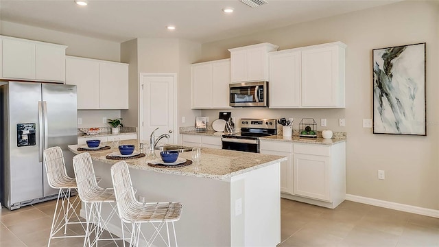 kitchen featuring an island with sink, a sink, stainless steel appliances, white cabinetry, and a kitchen bar