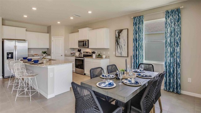 kitchen with white cabinets, stainless steel appliances, a kitchen bar, and a kitchen island with sink