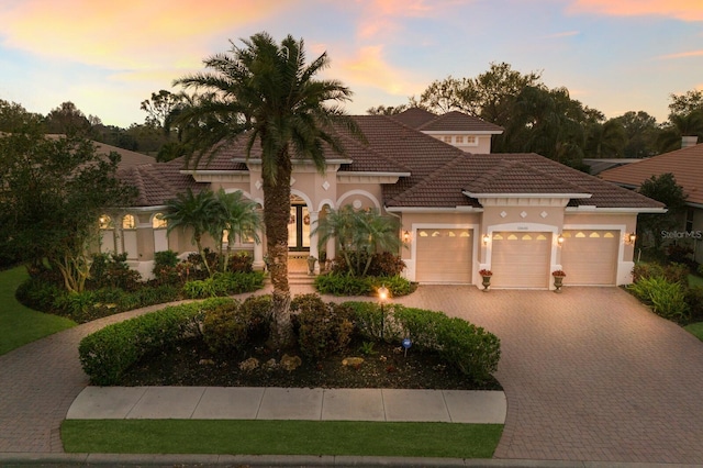 mediterranean / spanish home featuring decorative driveway, a tile roof, an attached garage, and stucco siding