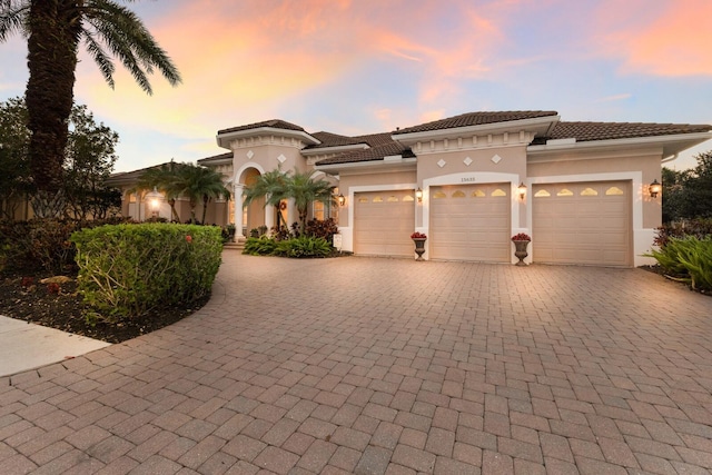 mediterranean / spanish-style home with decorative driveway, a garage, stucco siding, and a tile roof