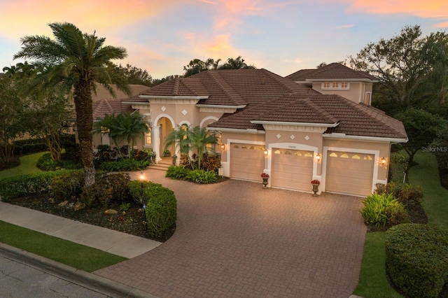 mediterranean / spanish home with a tile roof, decorative driveway, a garage, and stucco siding