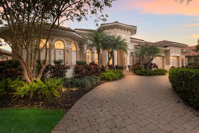 mediterranean / spanish-style home with decorative driveway, a garage, stucco siding, and a tiled roof