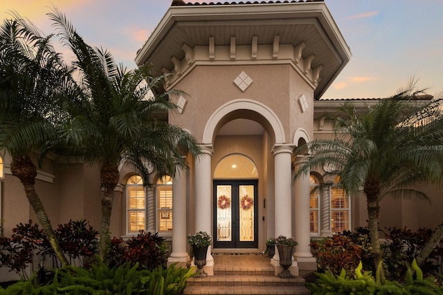 entrance to property with a tiled roof, stucco siding, and french doors